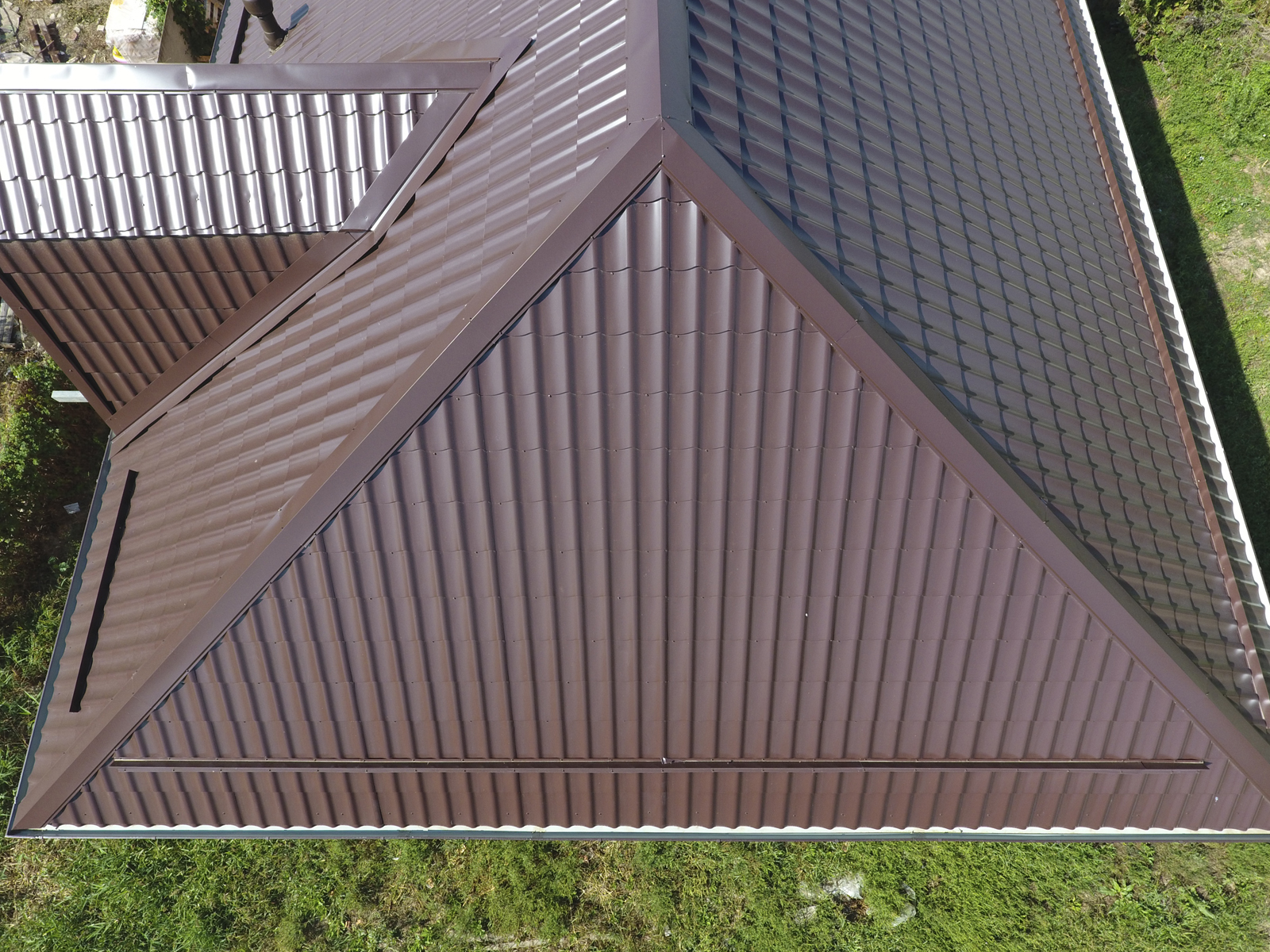 Aerial view of a brown metal roof with multiple triangular peaks, surrounded by green grass, showcasing the artistry of expert Metal Roofing Services.