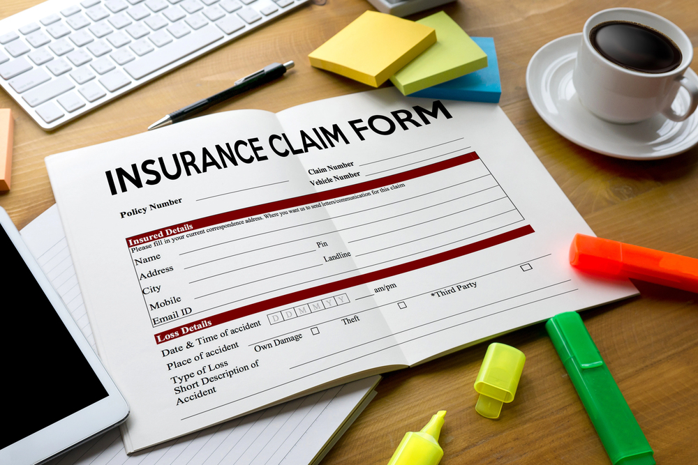 Open insurance claim form on a desk with a keyboard, sticky notes, coffee cup, and highlighters.
